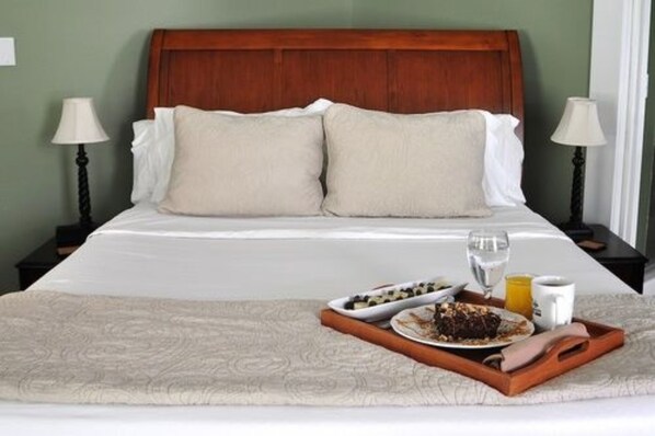 A neatly made bed with a wooden headboard, two bedside lamps, and a tray with breakfast items including a plate of food, a glass of water, and a cup. - Greenway House Bed & Breakfast (Green Lake)