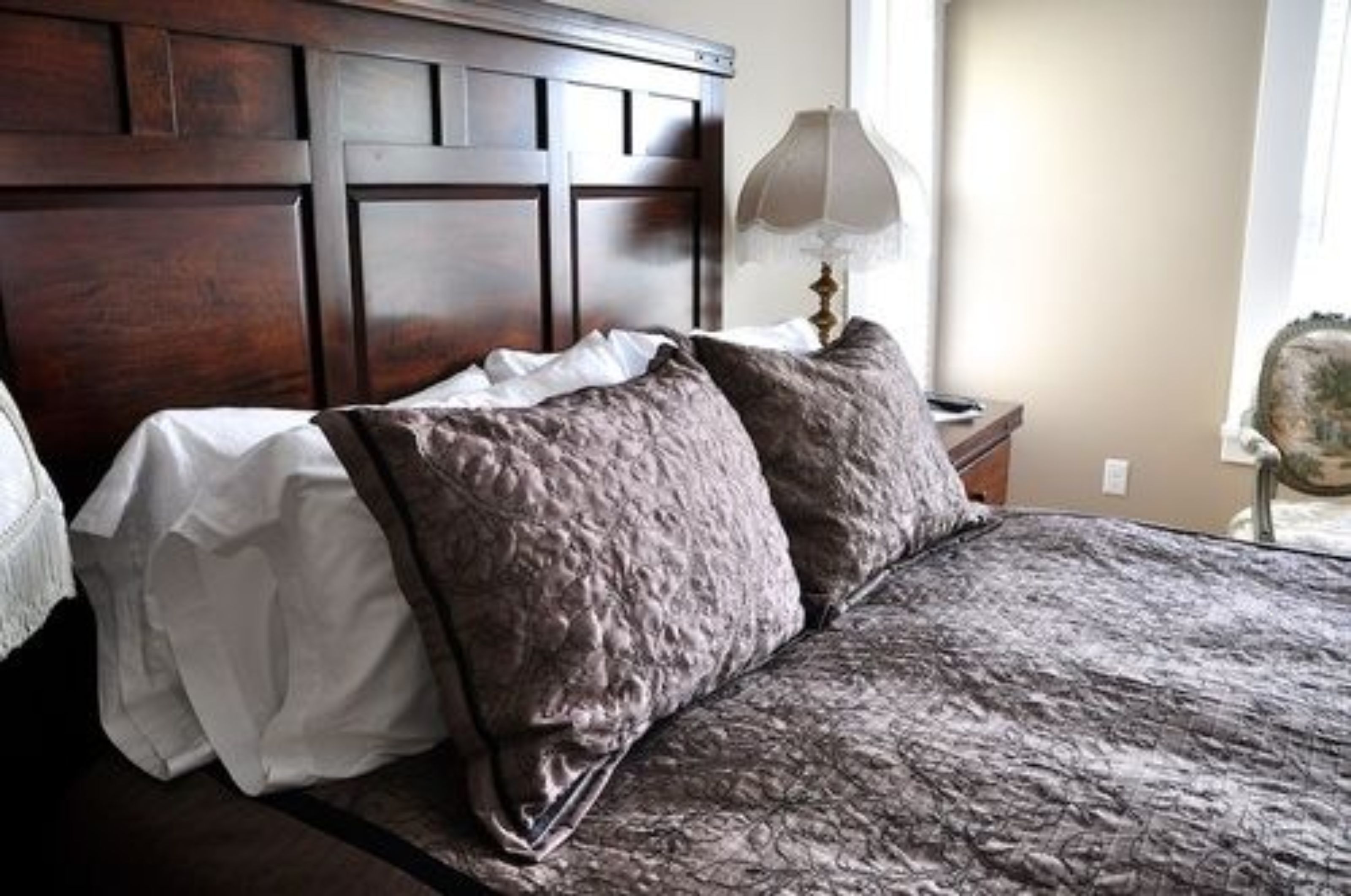 A bedroom with a wooden headboard, a bed with a patterned bedspread, and a bedside lamp.