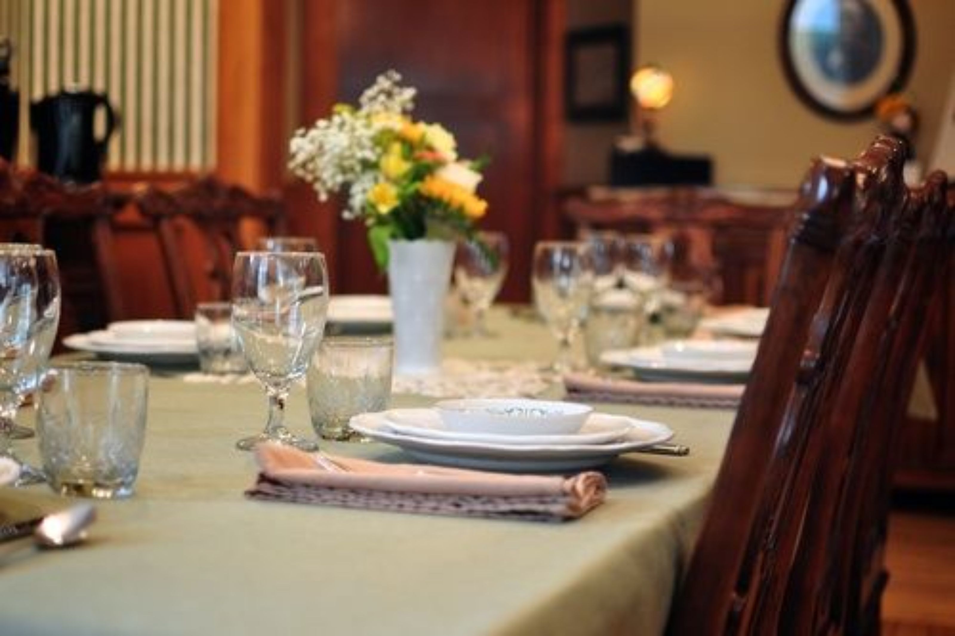 Una mesa de comedor preparada con platos, vasos y un florero.