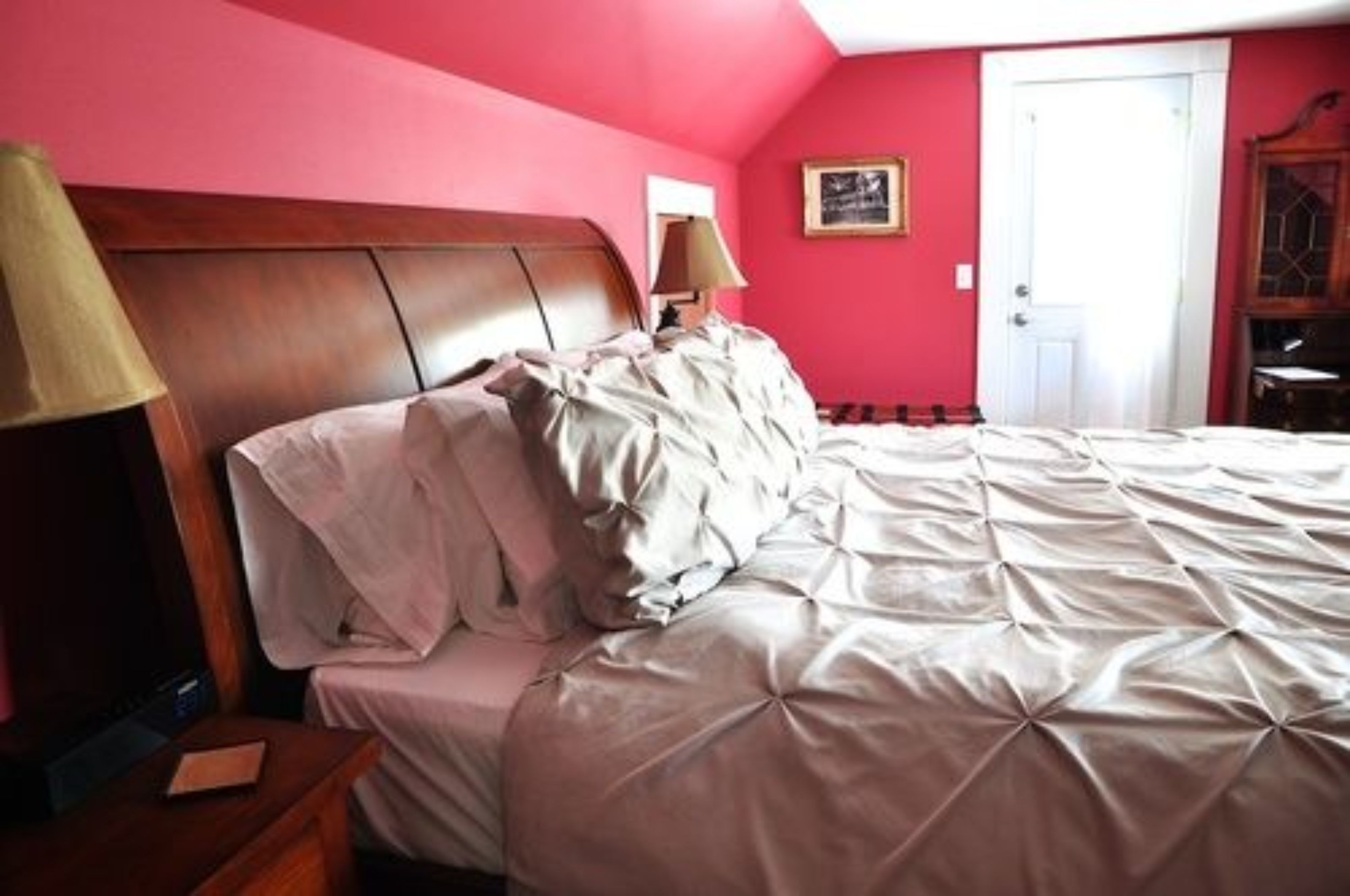 A bedroom with a bed, a nightstand, a lamp, a door, and a wall-mounted picture.