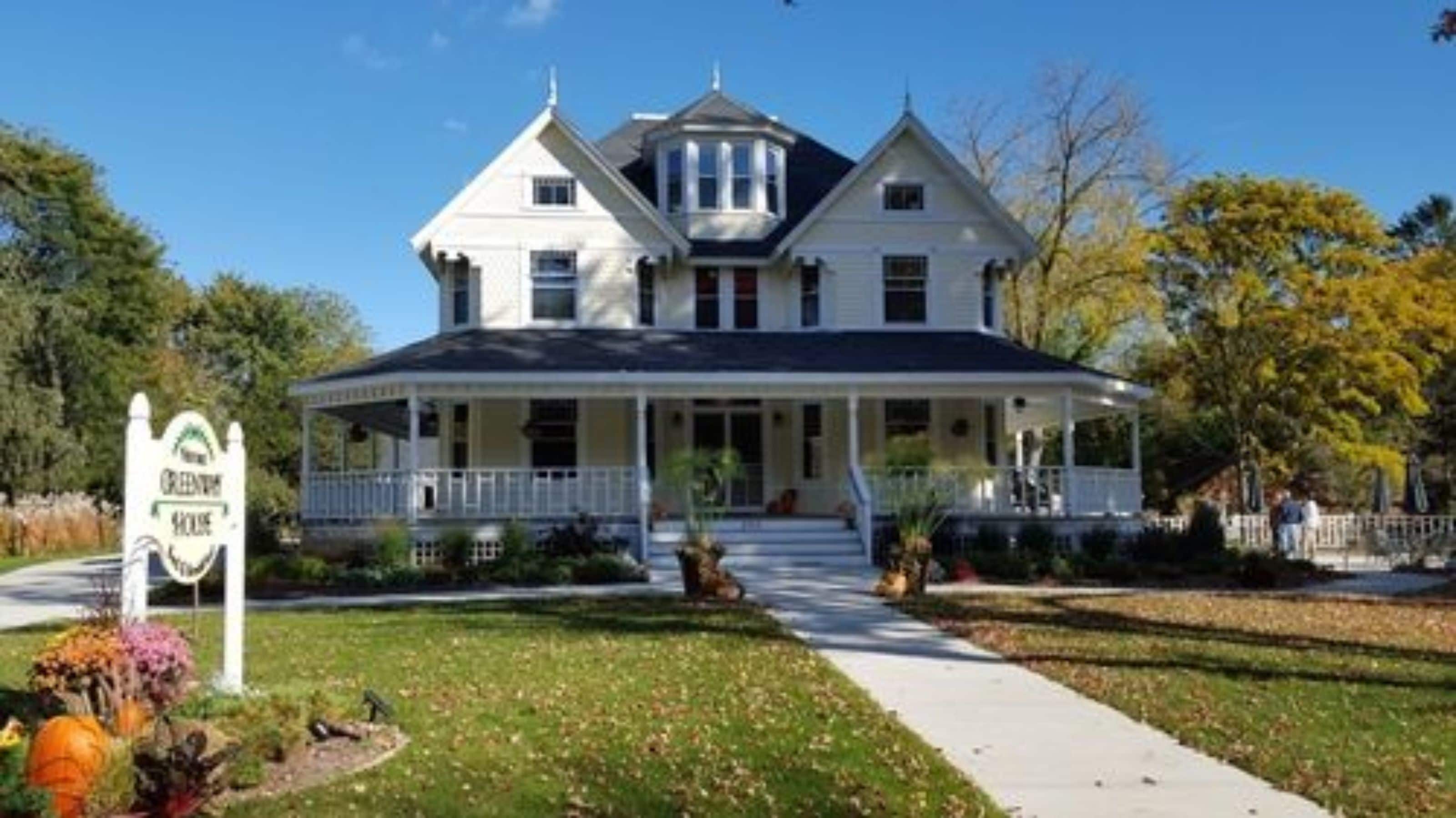 A large, two-story house with a porch and a sign that reads "Greenwood House".