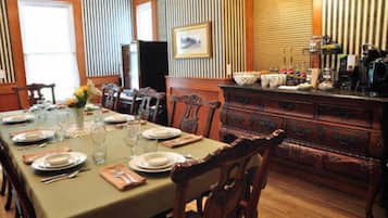 A dining room with a long table set for a meal, wooden chairs, a wooden cabinet with drawers, and a framed picture on the wall.