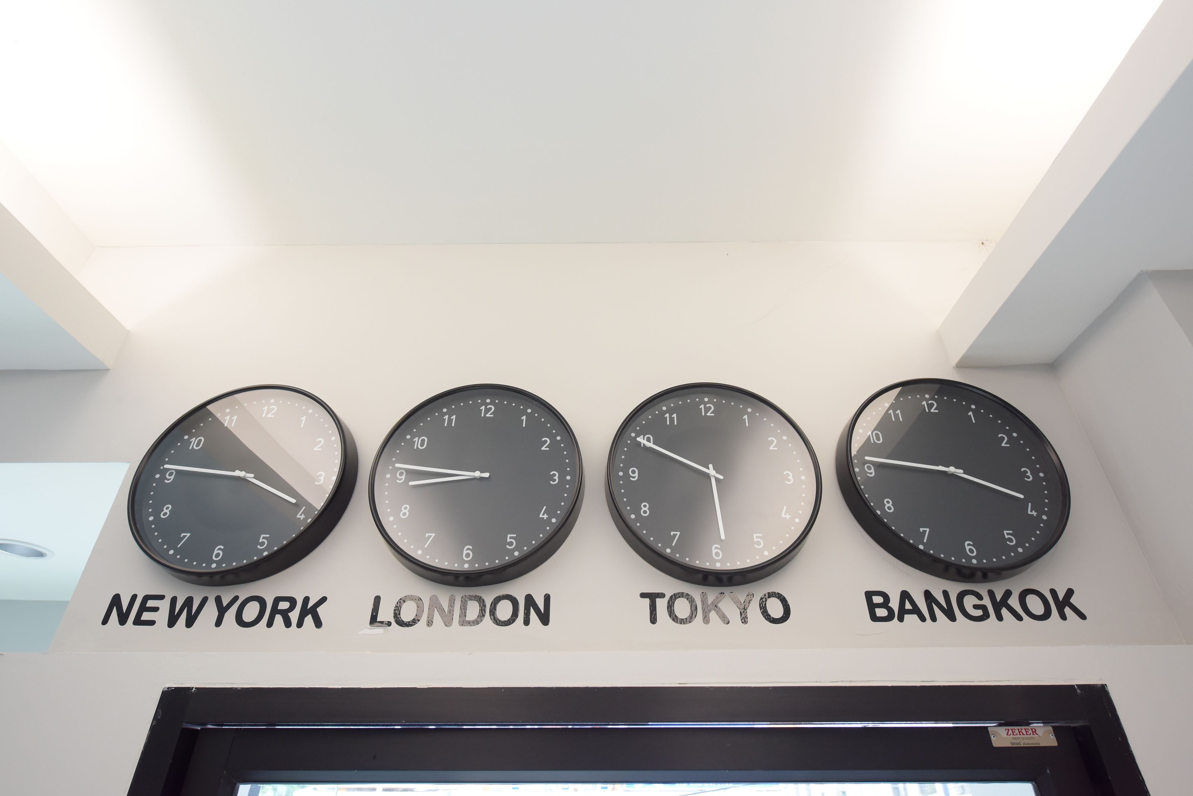 Vier Uhren, beschriftet mit Städtenamen: New York, London, Tokio und Bangkok.