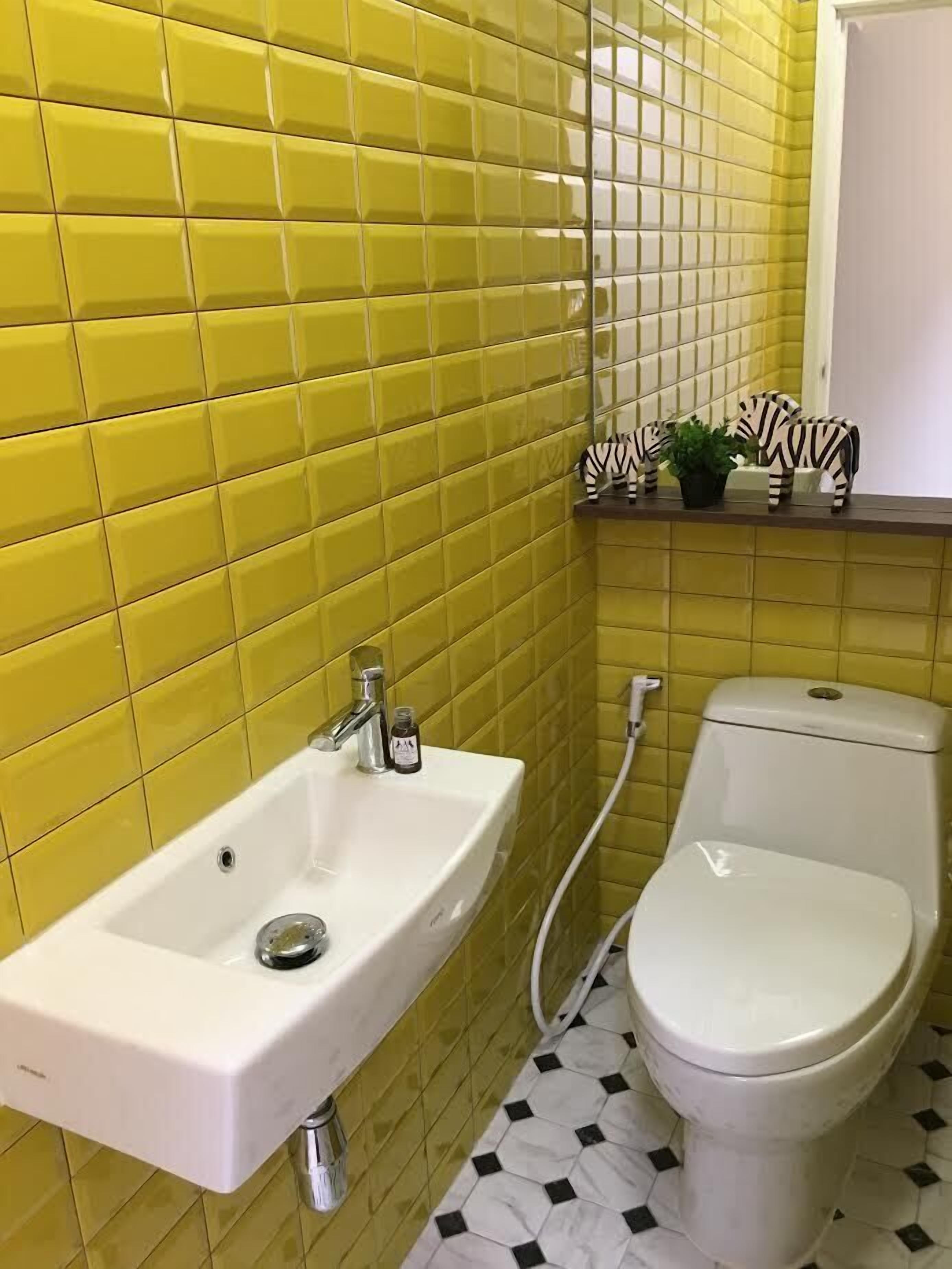 A bathroom with yellow tiled walls, a white sink, and a toilet.