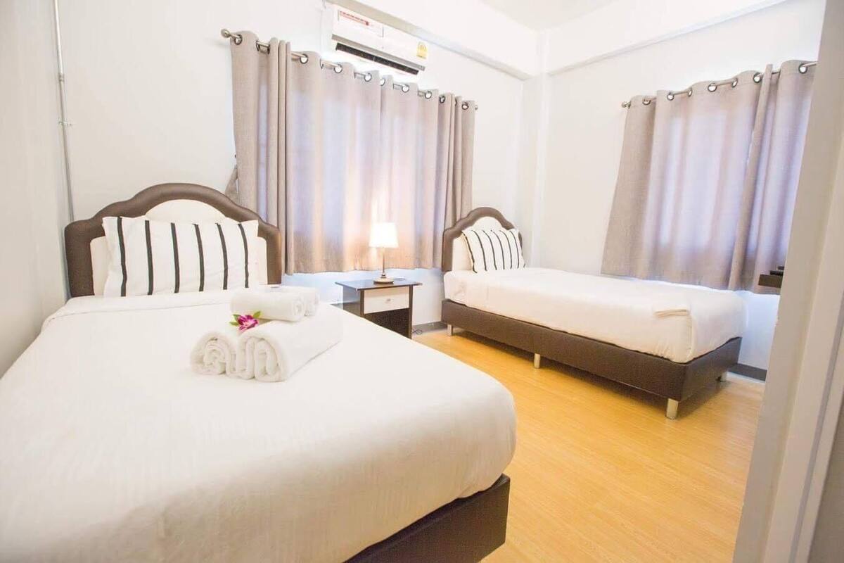 A hotel room with two beds, a nightstand, a lamp, and a window with curtains.