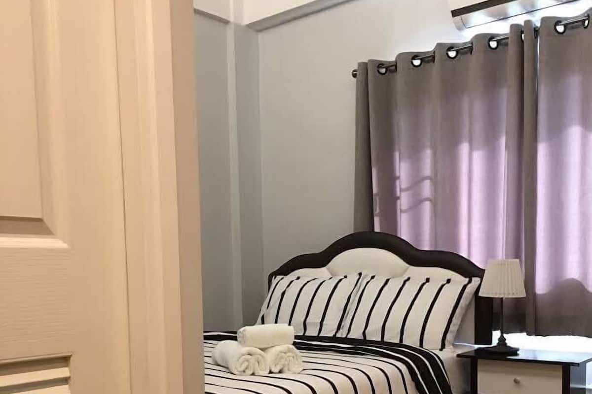 A neatly made bed with striped bedding, a bedside table with a lamp, and a bathroom with a shower curtain.