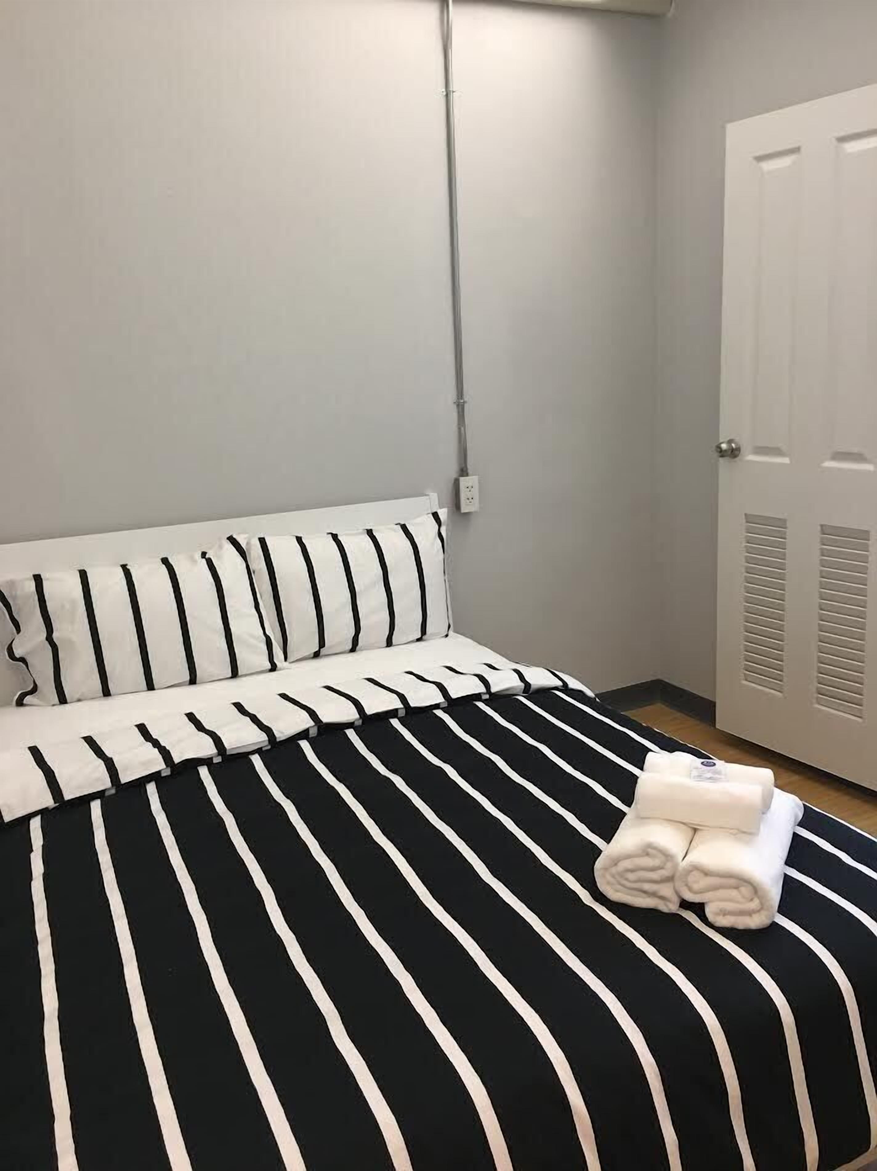 Una cama bien tendida con ropa de cama a rayas blancas y negras, una almohada blanca y toallas enrolladas sobre la cama.