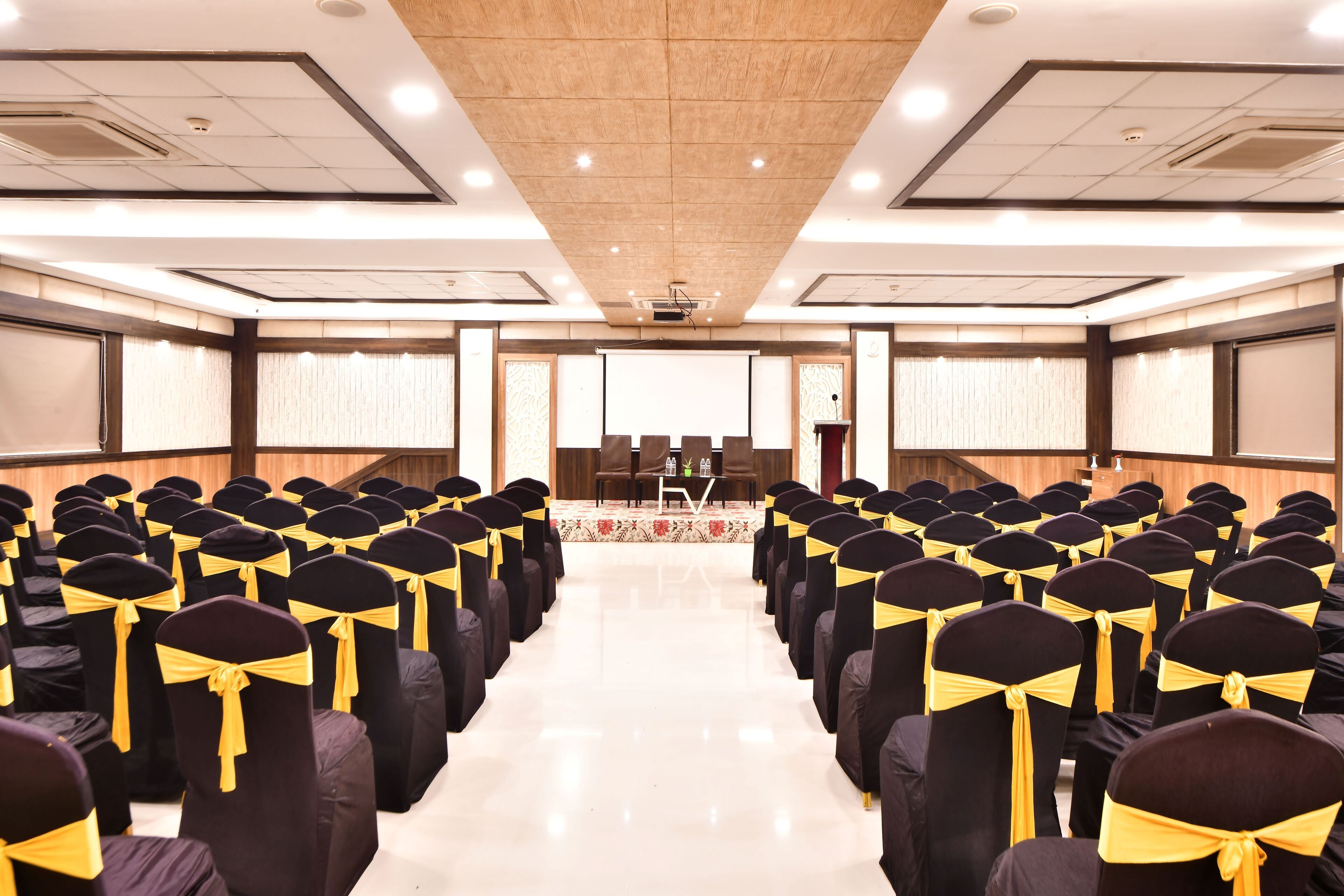 Un salón de conferencias con filas de sillas, un atril y una pantalla de proyección.