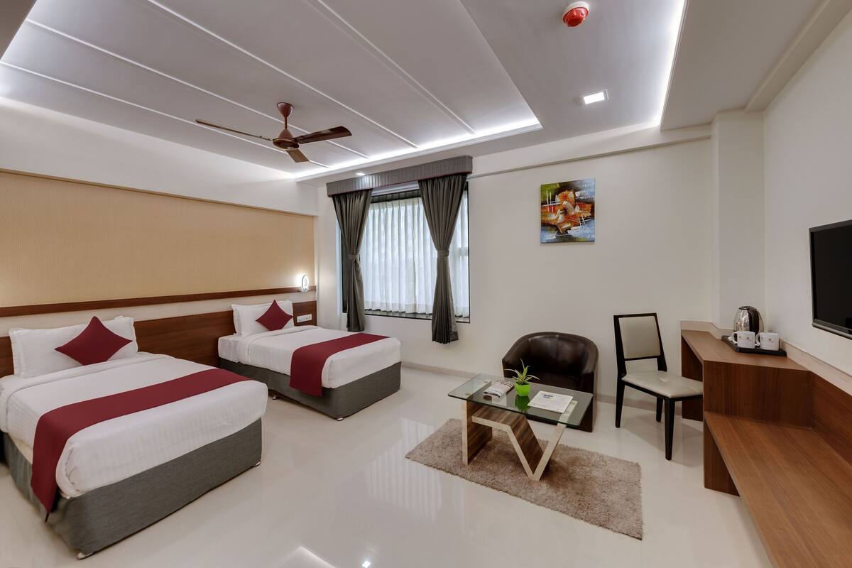 A modern hotel room with two beds, a desk, a chair, a TV, and a ceiling fan.