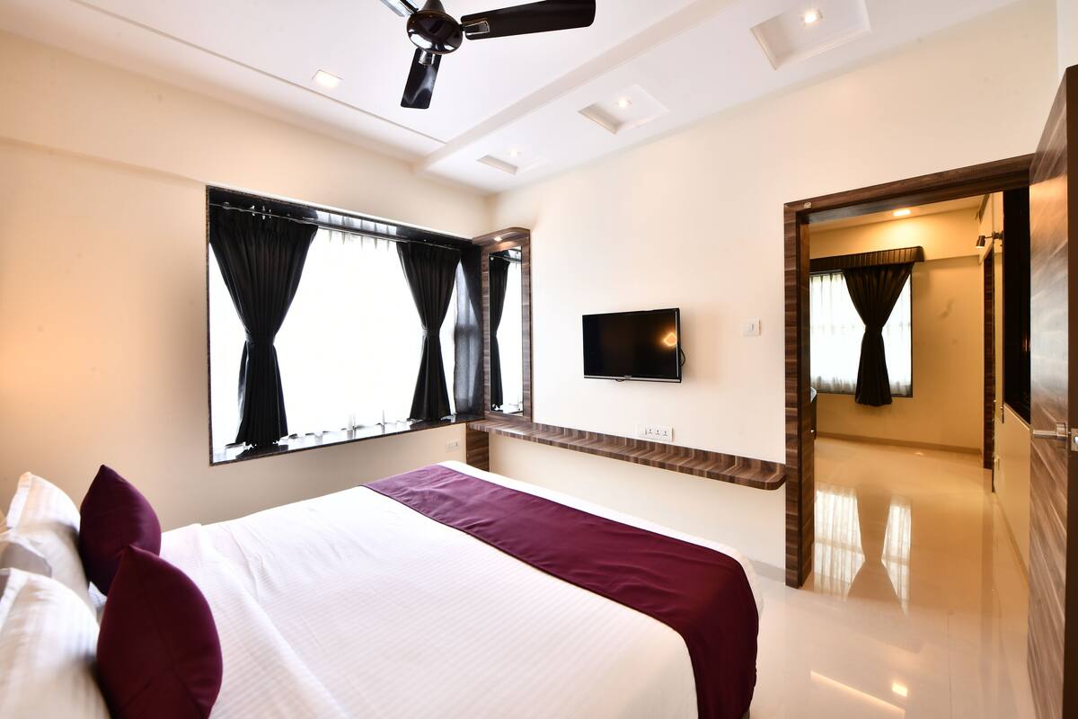 A hotel room with a bed, a flat-screen TV, a ceiling fan, and a large window with curtains.