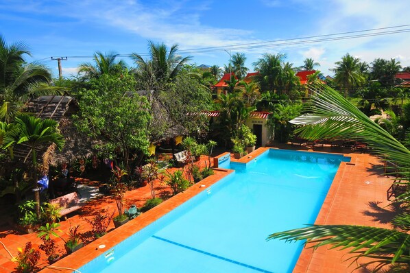 A swimming pool surrounded by lush greenery and palm trees, with a small building in the background.