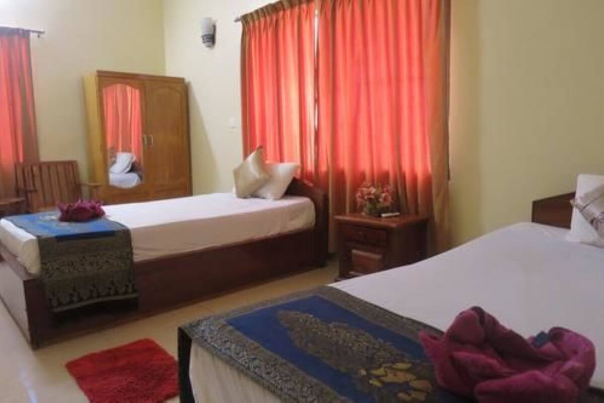 A hotel room with two beds, a wooden wardrobe, a small table, and a red rug.