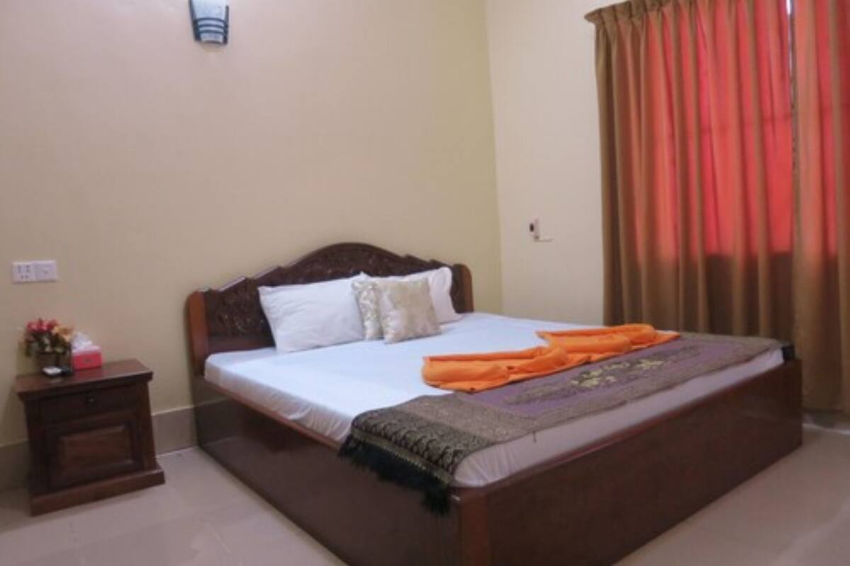 A bedroom with a wooden bed, white bedding, a nightstand with a lamp, and a window with curtains.