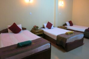 A hotel room with three single beds, each with a pillow and a small table beside it.