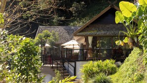A house with a stone roof, a staircase leading to a balcony, and outdoor seating with umbrellas.