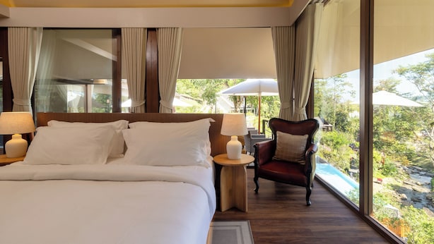 A bedroom with a large bed, a chair, a nightstand, and a view of a river.