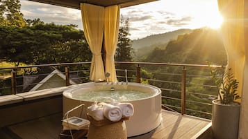 A hot tub on a wooden deck with a view of a valley and mountains.