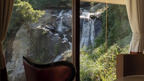 A room with a large window overlooking a waterfall and lush greenery.