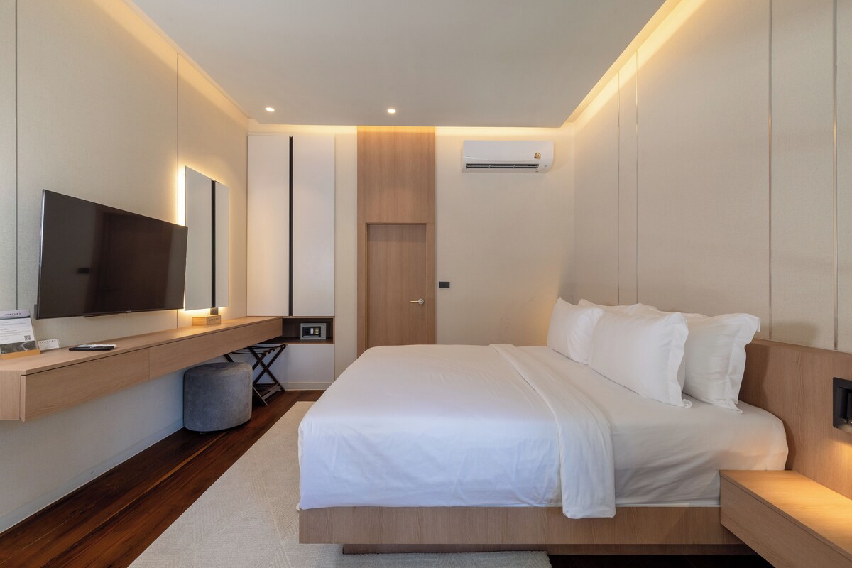 A modern bedroom with a bed, bedside tables, a TV, and an air conditioning unit.