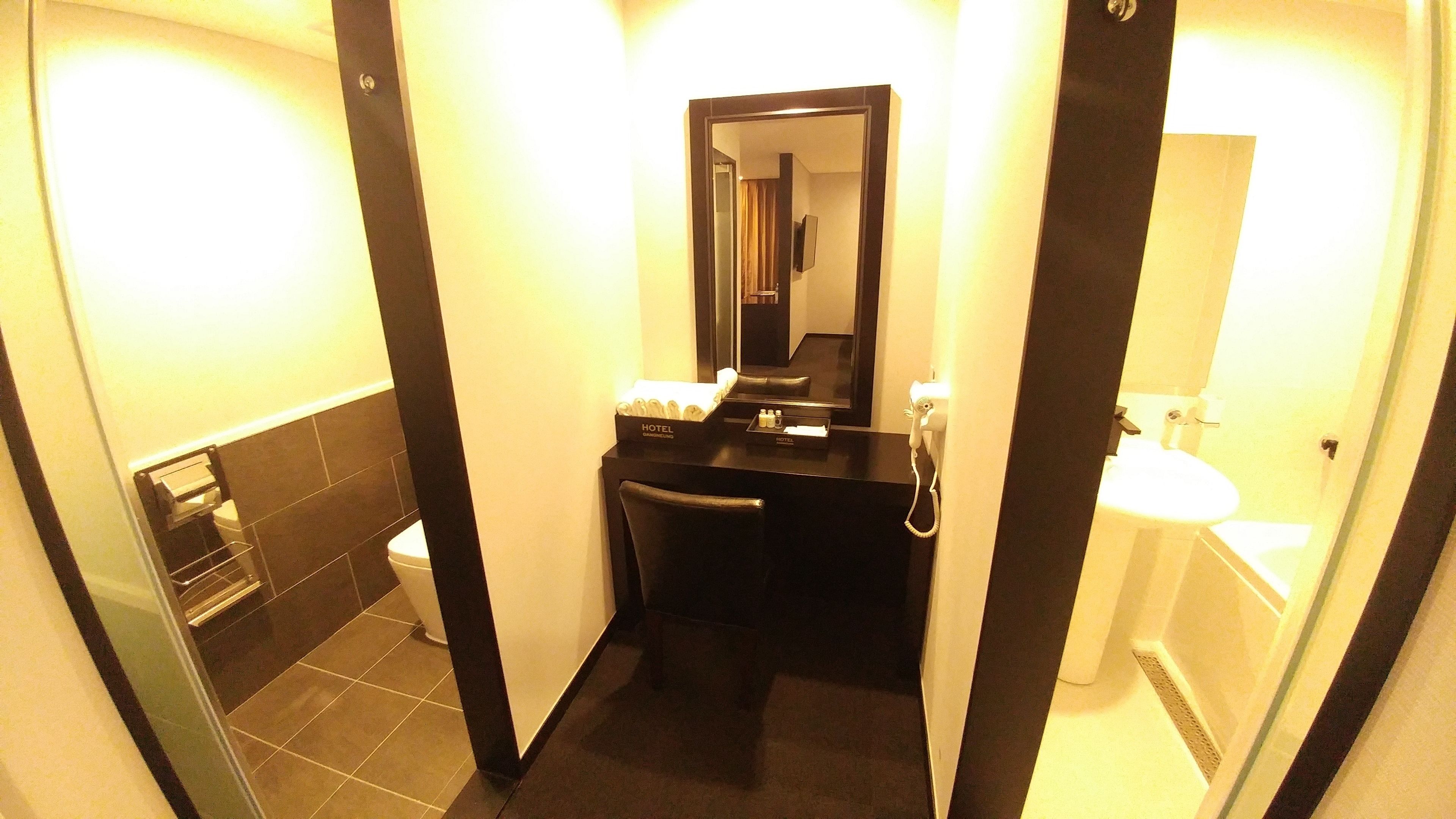 A compact hotel bathroom with a toilet, sink, and mirror.