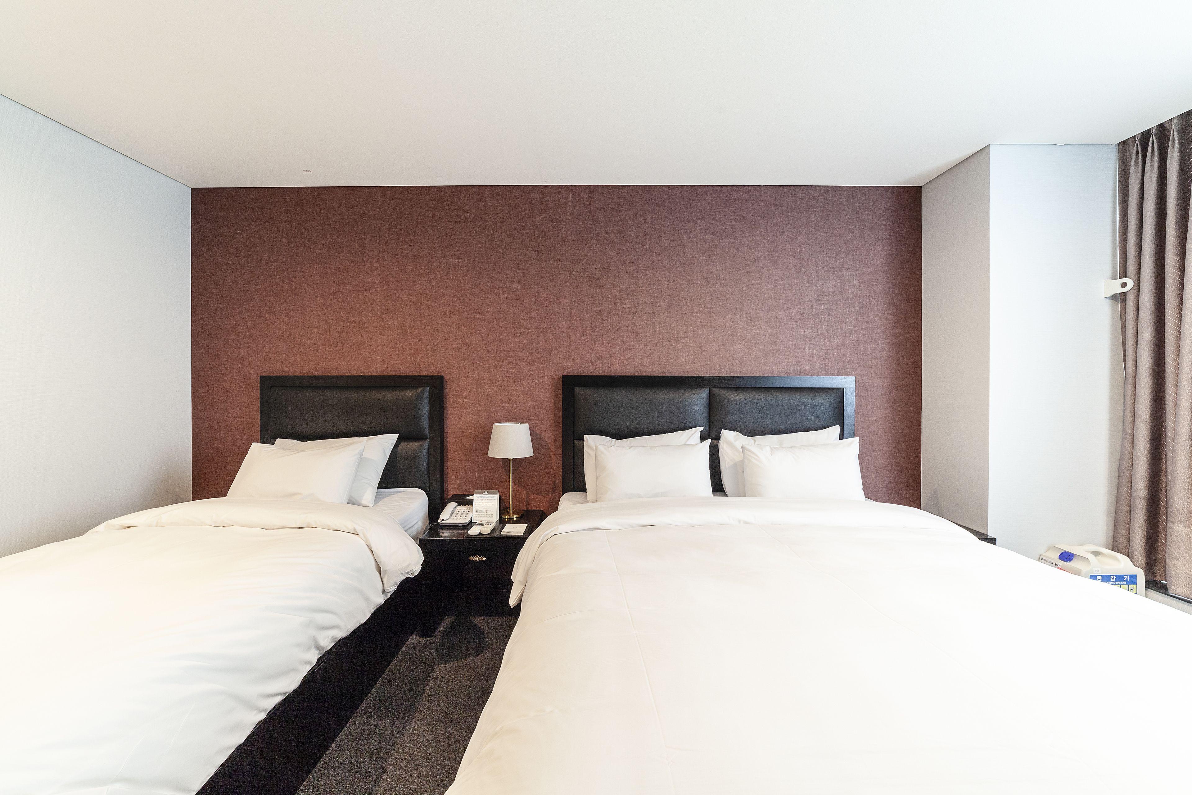 A hotel room with two single beds, a nightstand with a lamp, and a telephone.