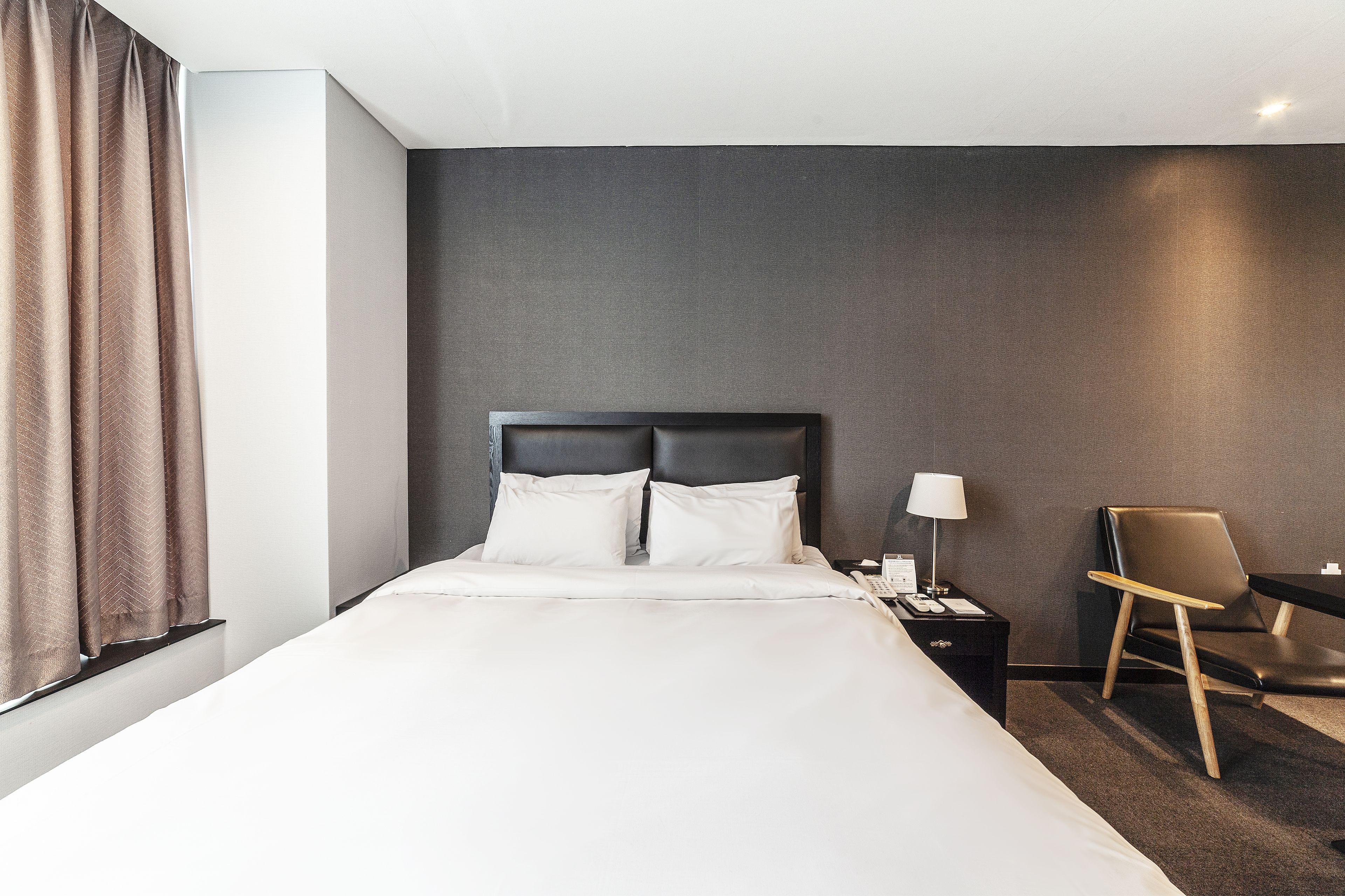 A hotel room with a large bed, a nightstand with a lamp, a chair, and a desk.