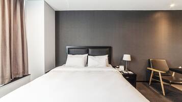 A hotel room with a large bed, a nightstand with a lamp, a chair, and a desk.
