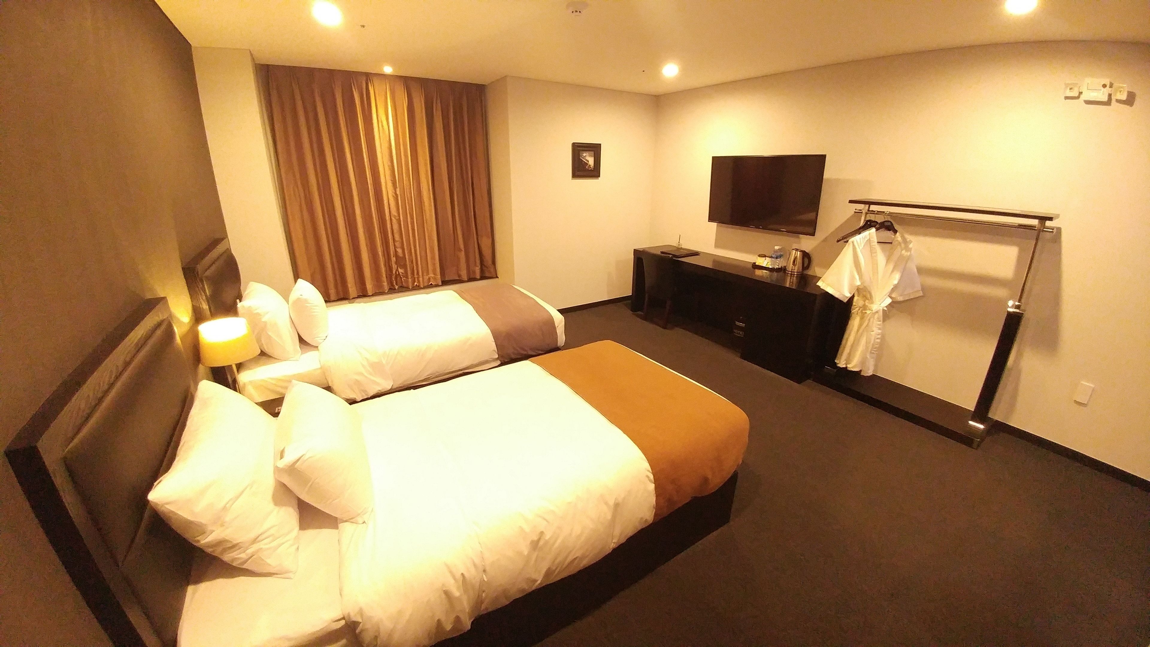 Ein Hotelzimmer mit zwei Betten, einem Schreibtisch, einem Fernseher und einem Bademantelständer.
