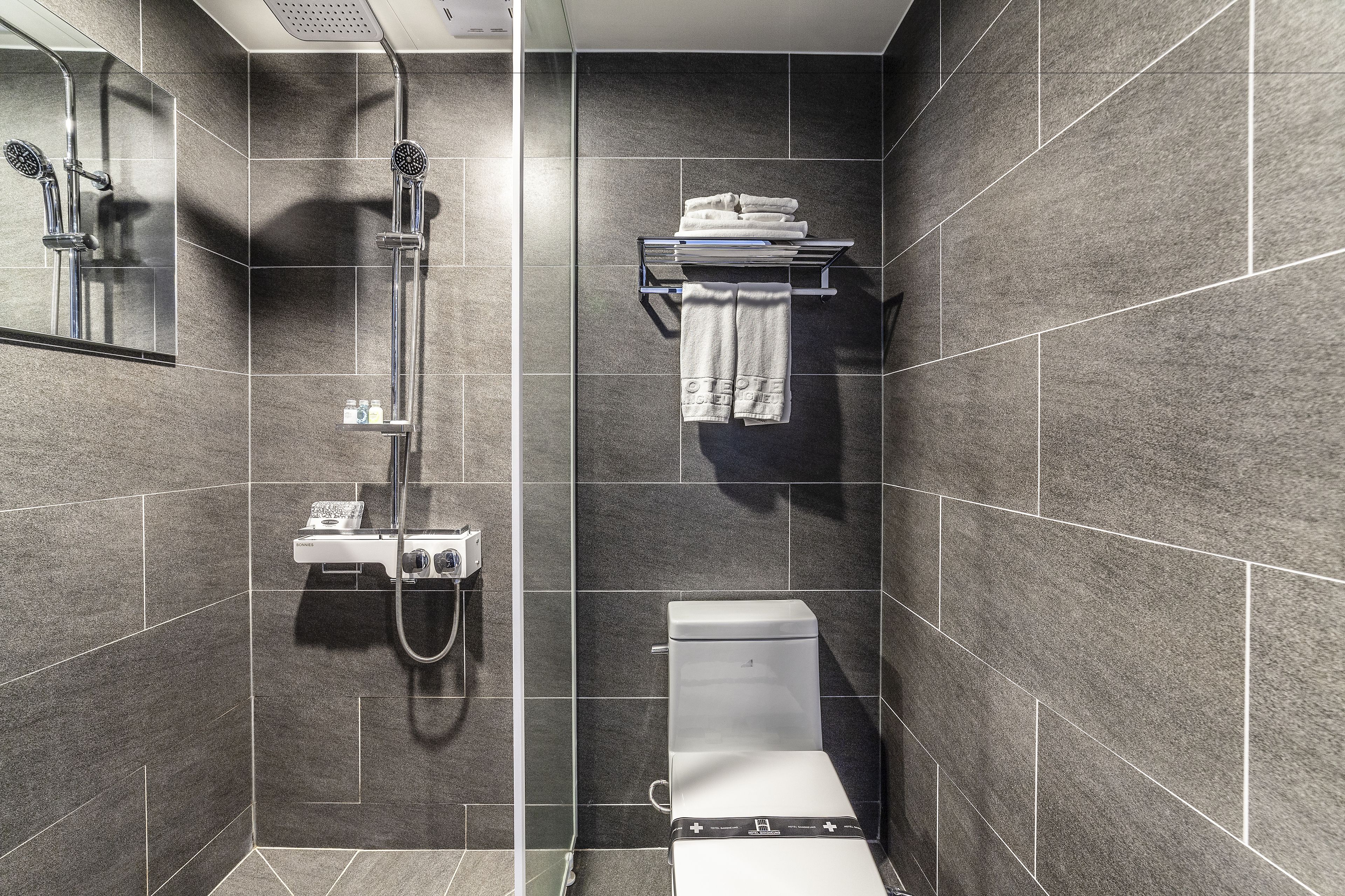 A modern bathroom with a shower, toilet, and towel rack.