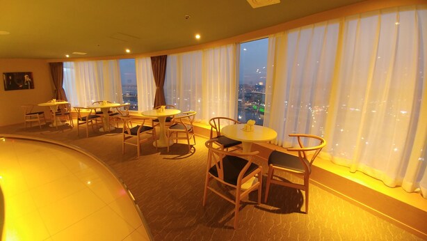 A hotel dining area with multiple round tables and chairs, large windows with curtains, and a view of the cityscape. - Gangneung Tourist Hotel (Gangneung)
