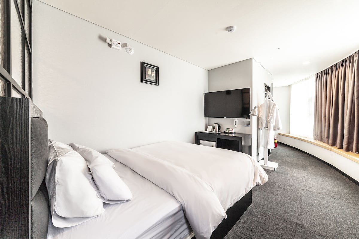Een hotelkamer met een bed, een bureau, een televisie en een raam met gordijnen.