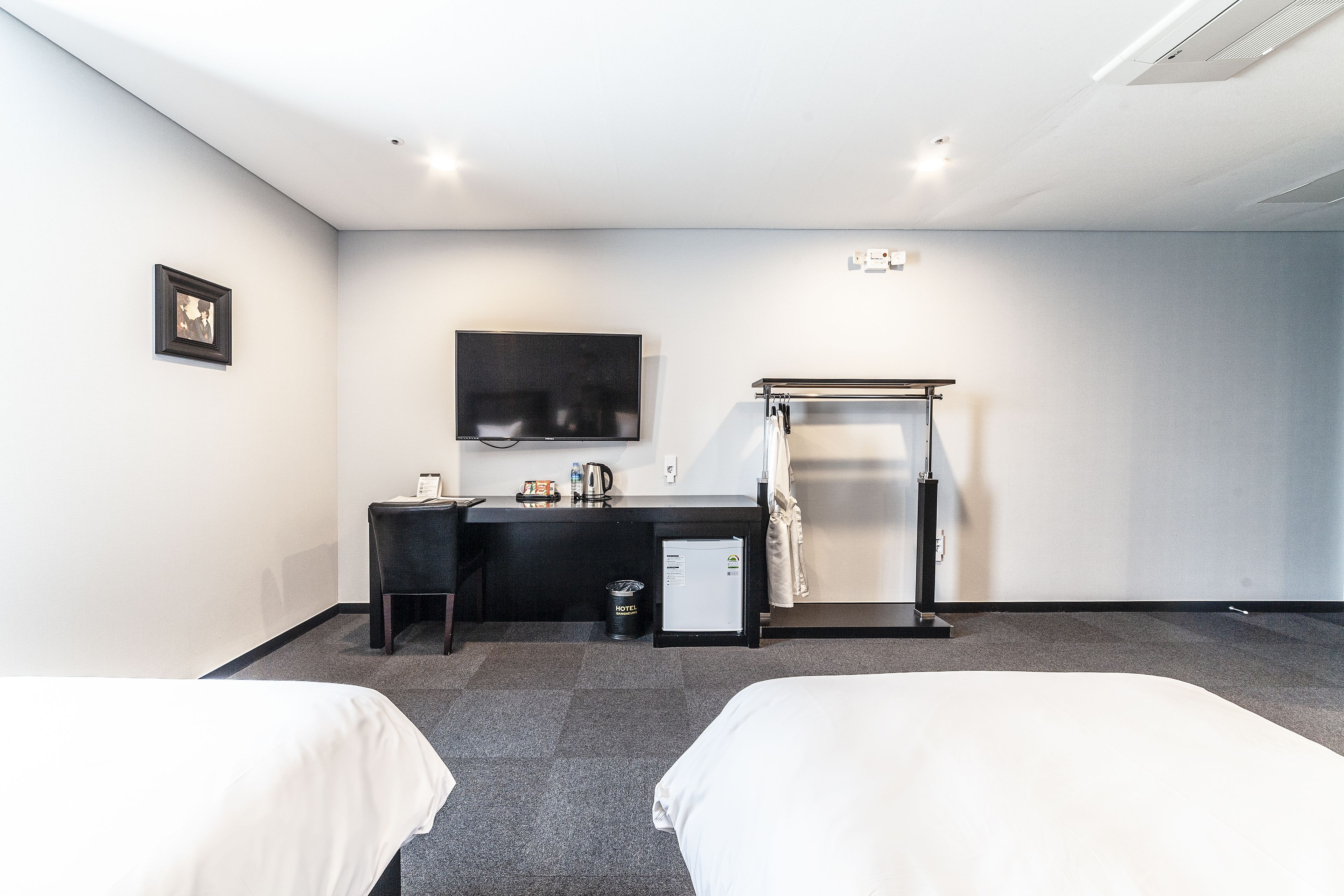 A hotel room with two beds, a desk, a TV, a mini-fridge, and a shower area.