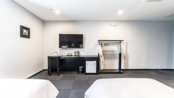 A hotel room with two beds, a desk, a TV, a mini-fridge, and a shower area.