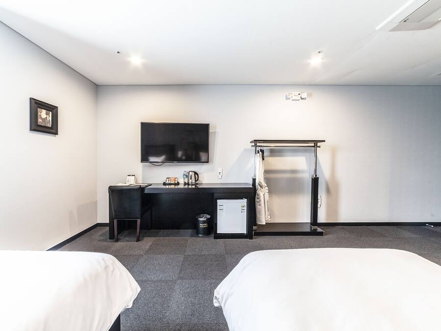 A hotel room with two beds, a desk, a TV, a mini-fridge, and a shower area.