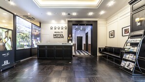 A hotel reception area with a dark wood floor, a reception desk, a waiting area with a black leather couch, and a wall with a welcome sign and a directory. - Gangneung Tourist Hotel (Gangneung)