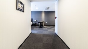A hallway with a checkered carpet, a framed picture on the wall, a desk with a chair, and a wall-mounted air vent. - Gangneung Tourist Hotel (Gangneung)