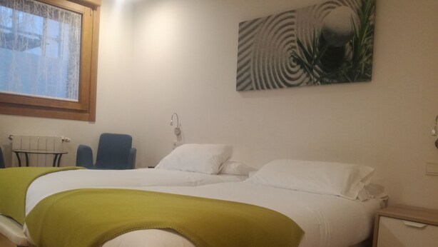 A hotel room with a bed, a chair, a nightstand, and a painting on the wall. - Pensión El Paseo (Pamplona)