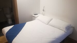 A bedroom with a bed, a bedside table, and a nightstand. - Pensión El Paseo (Pamplona)