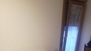A bed with white and blue bedding, a wooden door with a window, and a chair with a patterned cover. - Pensión El Paseo (Pamplona)