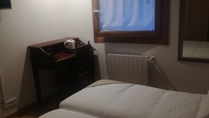 A hotel room with two beds, a desk with a chair, a window with curtains, an air conditioning unit, and a radiator. - Pensión El Paseo (Pamplona)
