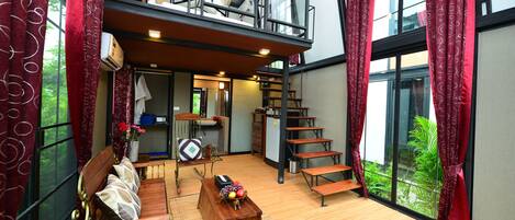 A spacious living area with a wooden floor, a sofa, a coffee table, and a staircase leading to an upper level.