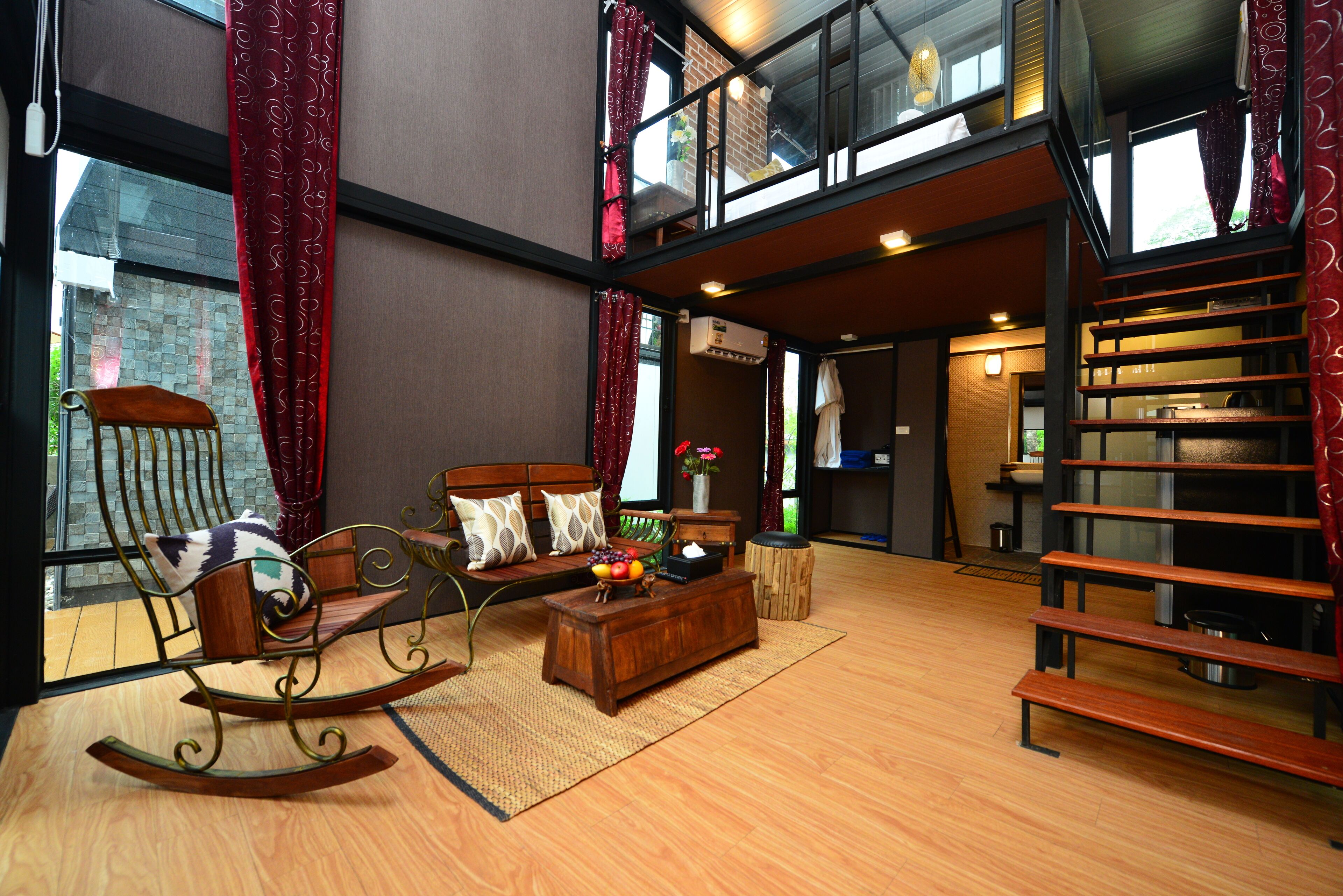 A spacious living area with a wooden rocking chair, a sofa, and a coffee table. A staircase leads to an upper level.