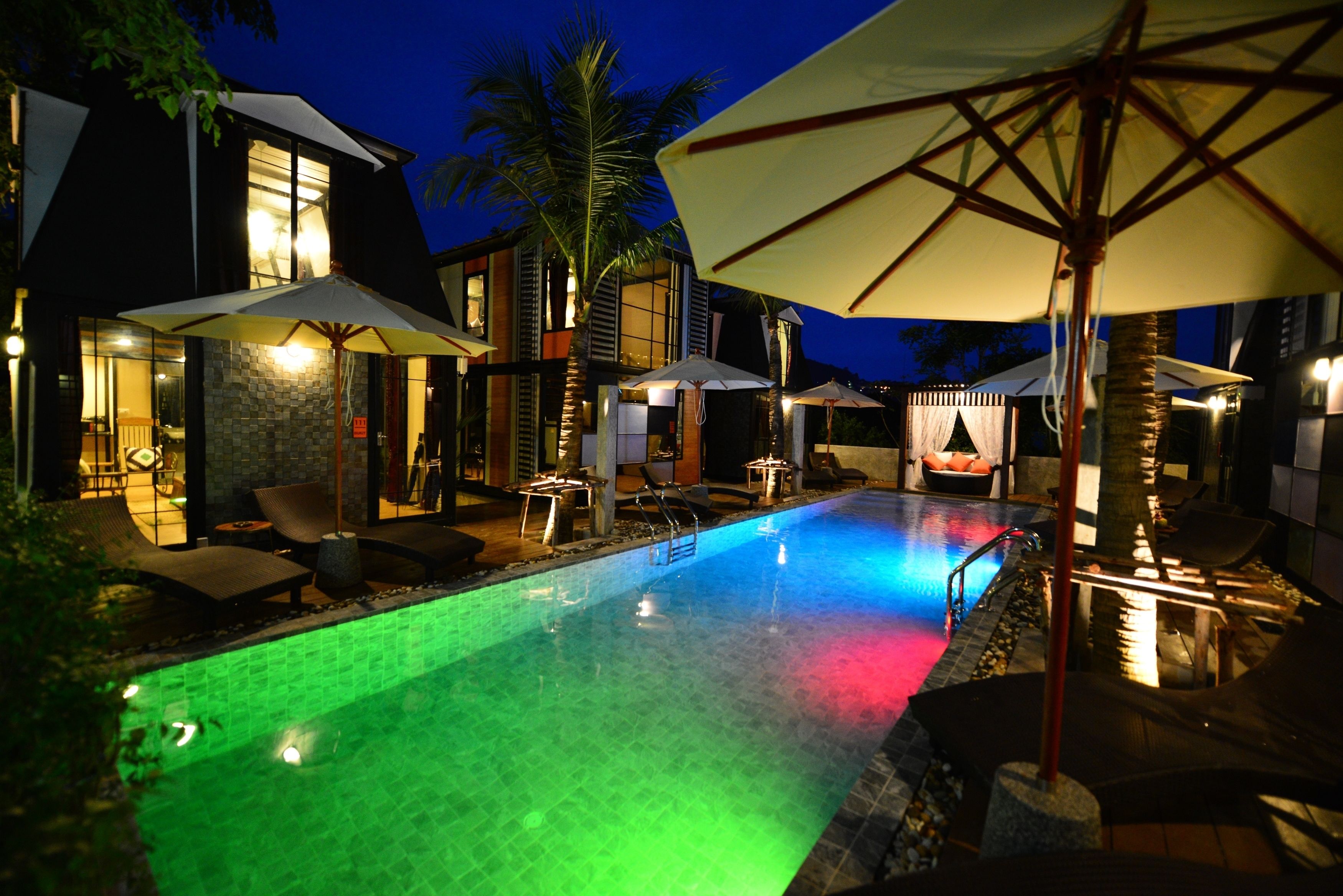 Una piscina con un'esposizione di luci colorate, circondata da lettini e ombrelloni, con una casa moderna sullo sfondo.