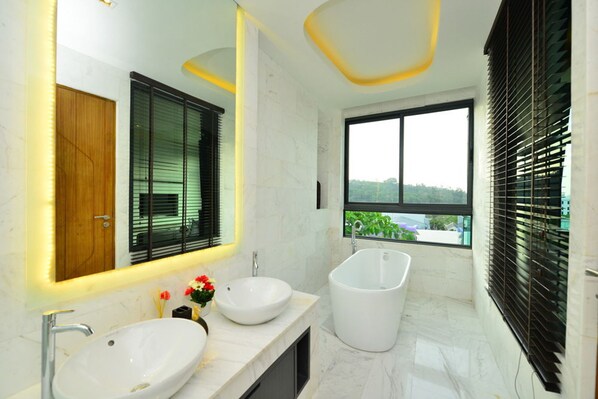 A modern bathroom with two sinks, a bathtub, and a large window with blinds. - Bukit Pool Villas (Patong)