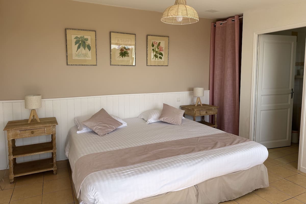 A bedroom with a large bed, two bedside tables, a hanging light fixture, and three framed pictures on the wall.