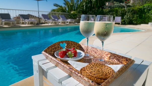Un cadre agréable au bord de la piscine, avec des chaises longues, un plateau sur lequel se trouve une assiette de fraises et deux verres de vin blanc.