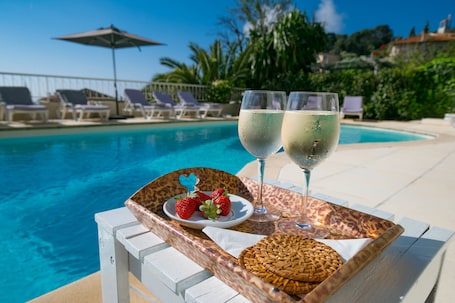 A poolside setting with lounge chairs, a tray with a plate of strawberries, and two glasses of white wine.