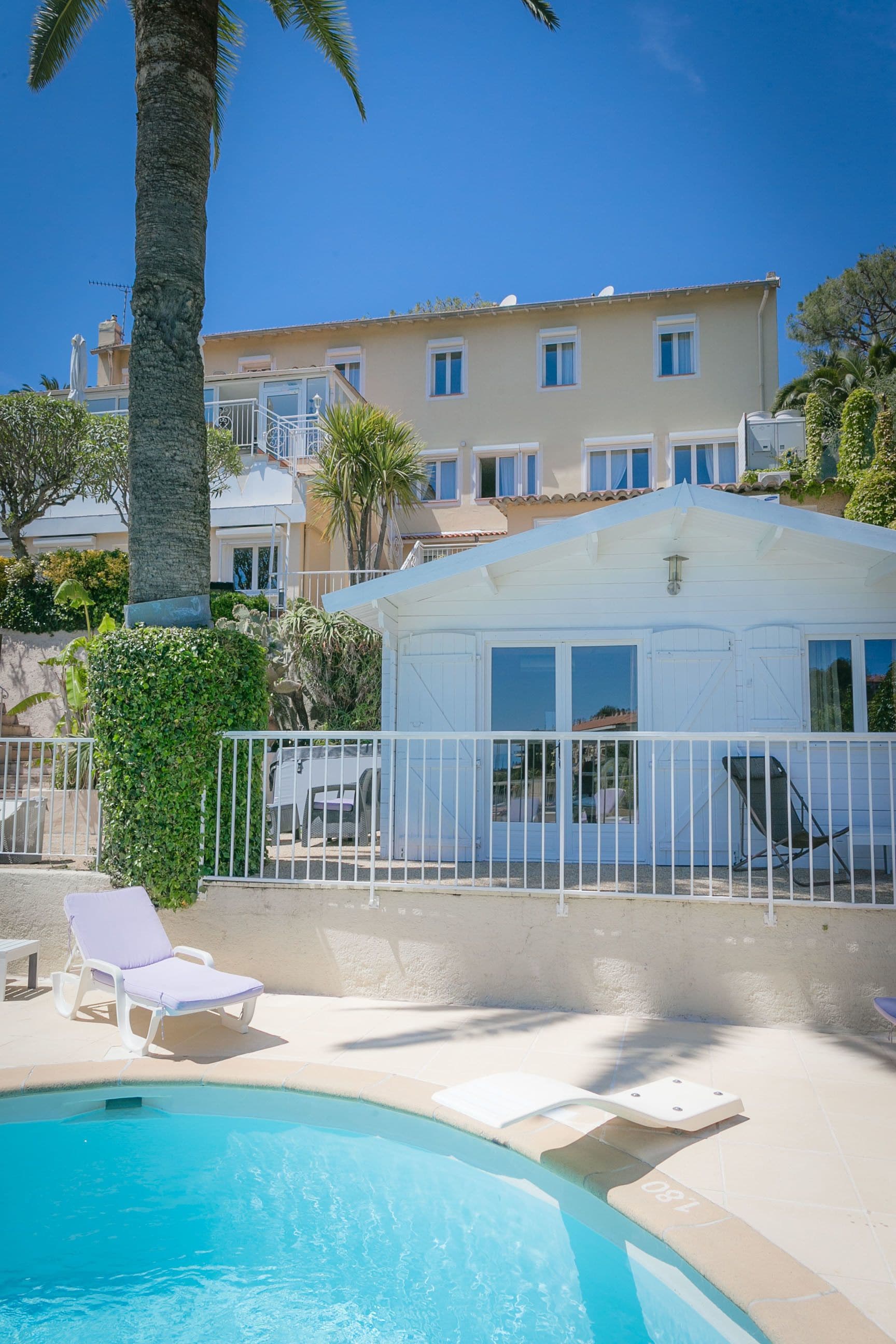 A pool area with lounge chairs, a white building, and a palm tree.