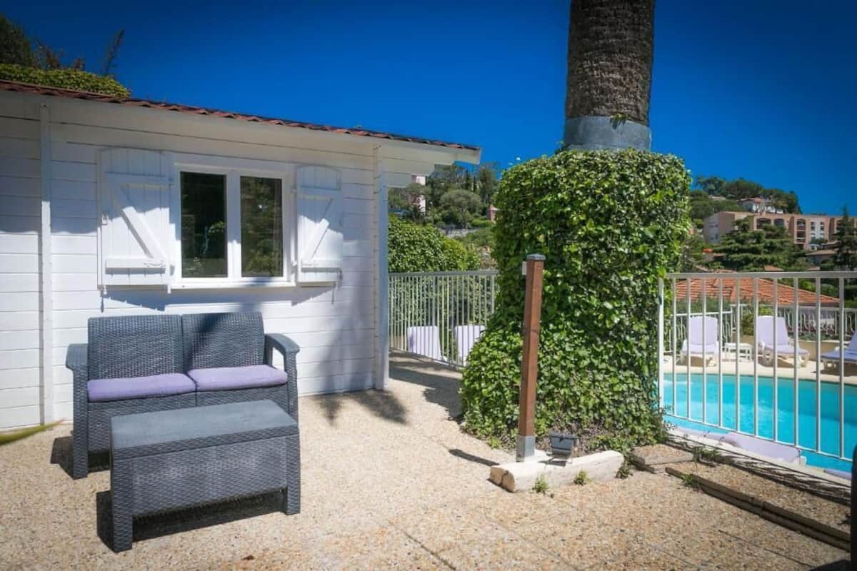 A patio with wicker furniture, a white building, a tree, and a pool.