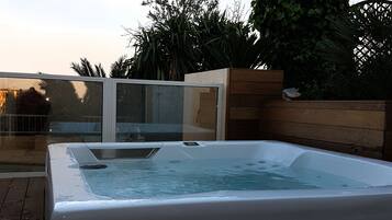Un jacuzzi en una terraza de madera, con recinto de vidrio y una valla de madera al fondo.